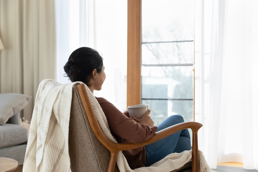 Woman taking a calm breath with a cup of tea by a sunny window