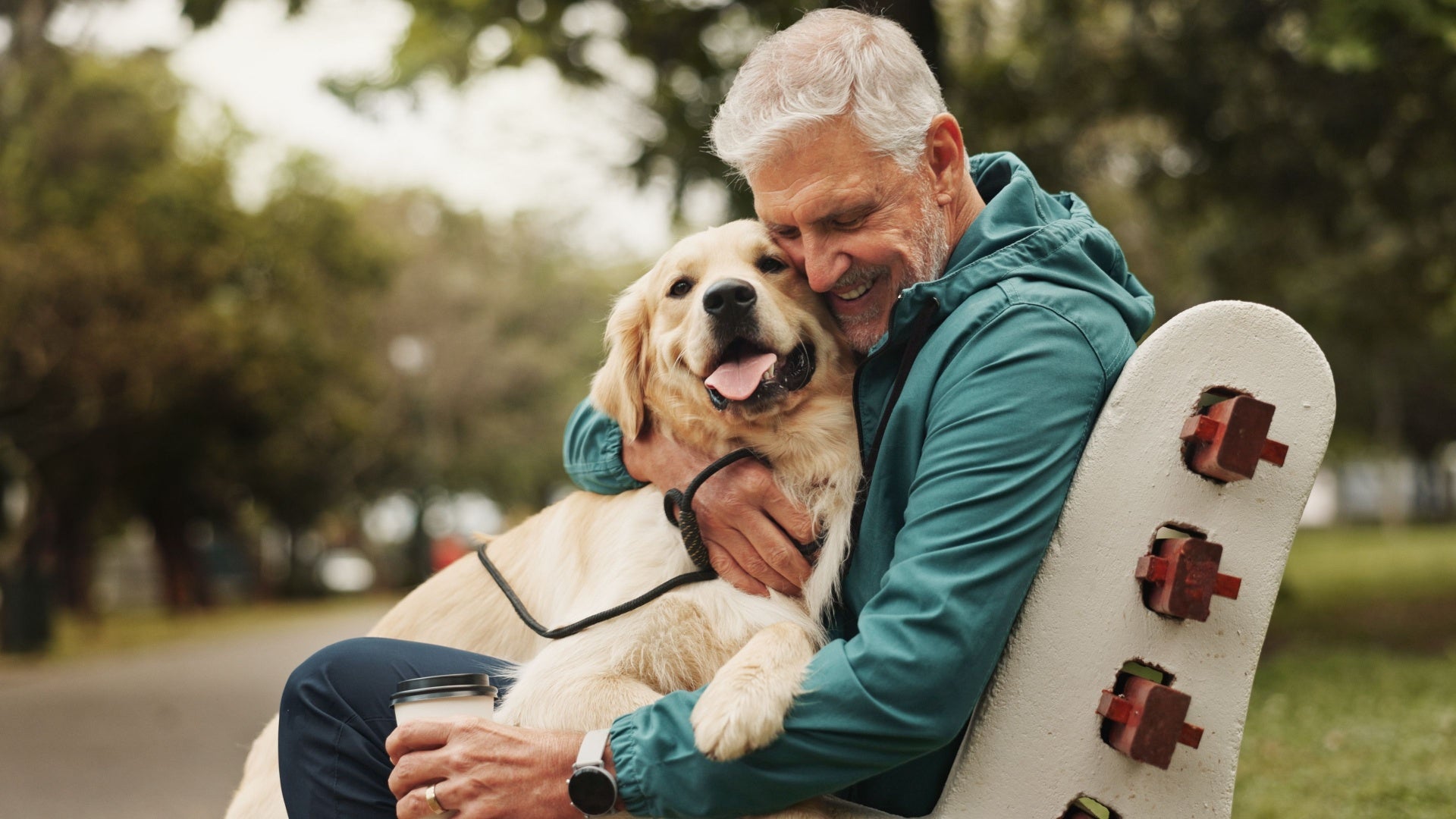 Man hugging a dog in a park with trees in the background